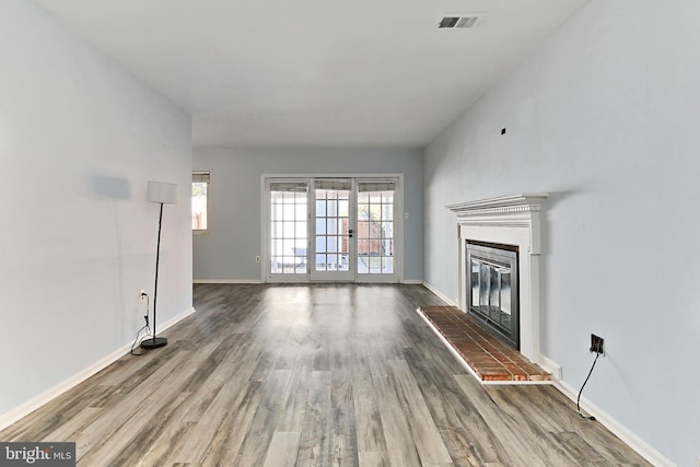 unfurnished living room with visible vents, a brick fireplace, baseboards, french doors, and wood finished floors