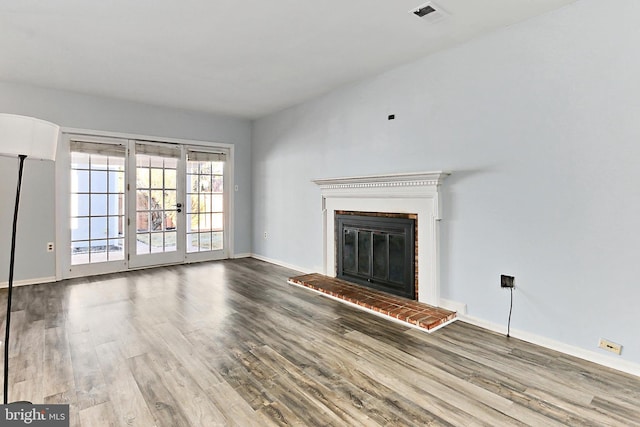 unfurnished living room with visible vents, baseboards, a brick fireplace, and wood finished floors