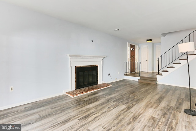 unfurnished living room with visible vents, a brick fireplace, baseboards, stairway, and wood finished floors