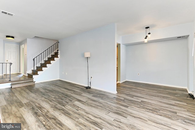 unfurnished living room featuring visible vents, baseboards, wood finished floors, and stairway