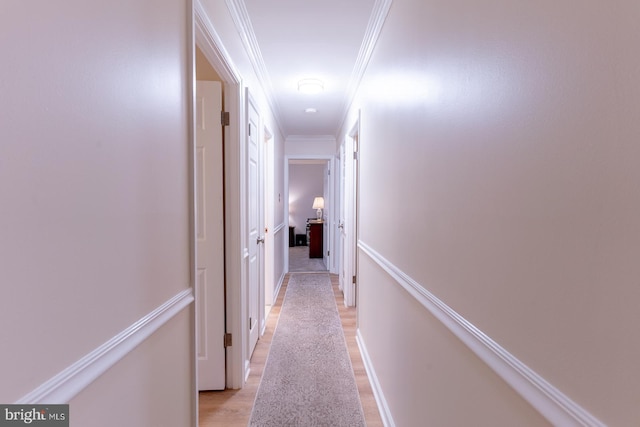 corridor featuring baseboards, crown molding, and light wood finished floors