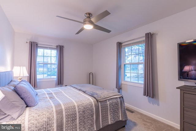 bedroom featuring a ceiling fan, light carpet, baseboards, and multiple windows