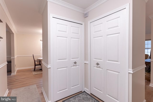 hall with light wood-style flooring, ornamental molding, and baseboards