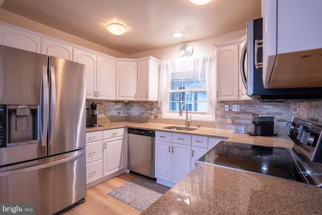 kitchen featuring light stone counters, stainless steel appliances, light wood-style flooring, white cabinetry, and a sink