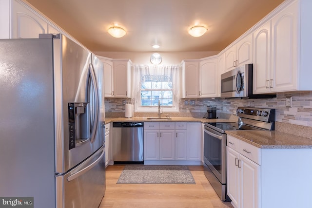 kitchen with light wood-type flooring, appliances with stainless steel finishes, white cabinets, and a sink