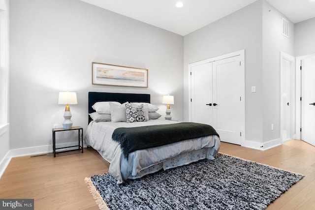 bedroom with a closet, wood finished floors, visible vents, and baseboards