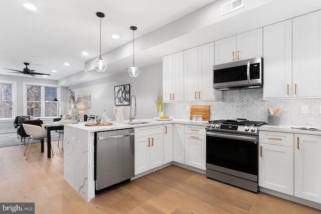 kitchen with stainless steel appliances, light countertops, white cabinets, and hanging light fixtures