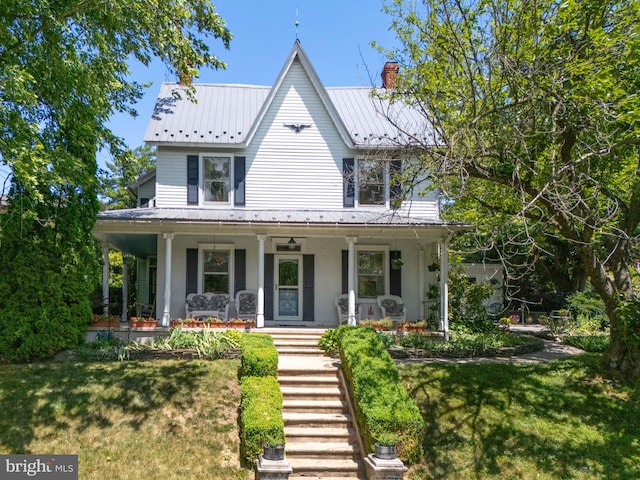 view of front of property featuring metal roof, a porch, a front lawn, and a chimney