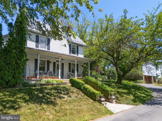 view of front of property with a porch, a front lawn, a chimney, and brick siding