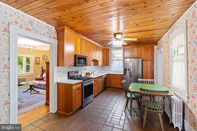 kitchen with light countertops, appliances with stainless steel finishes, brown cabinets, radiator heating unit, and wallpapered walls