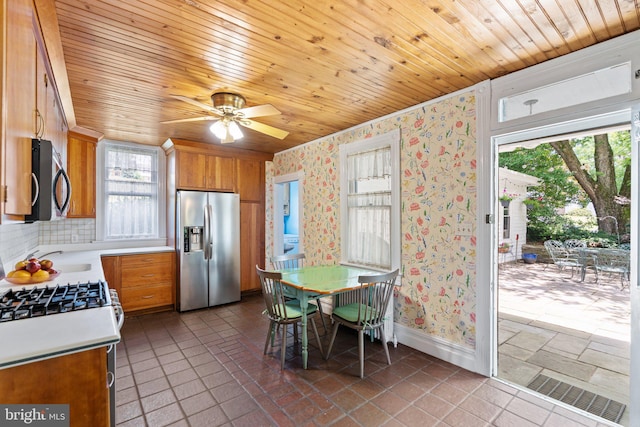 kitchen featuring wallpapered walls, stainless steel appliances, light countertops, and brown cabinetry