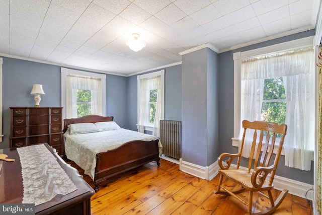 bedroom with radiator, crown molding, baseboards, and wood finished floors