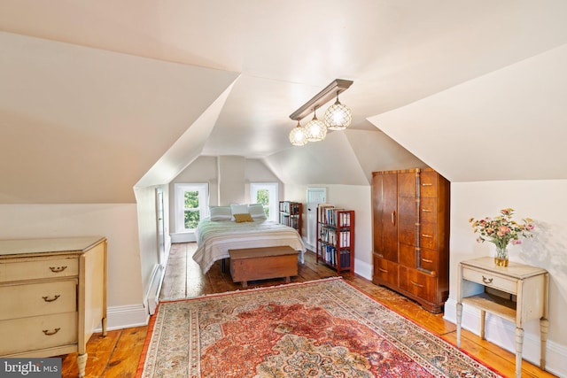 bedroom featuring lofted ceiling, a baseboard radiator, wood finished floors, and baseboards