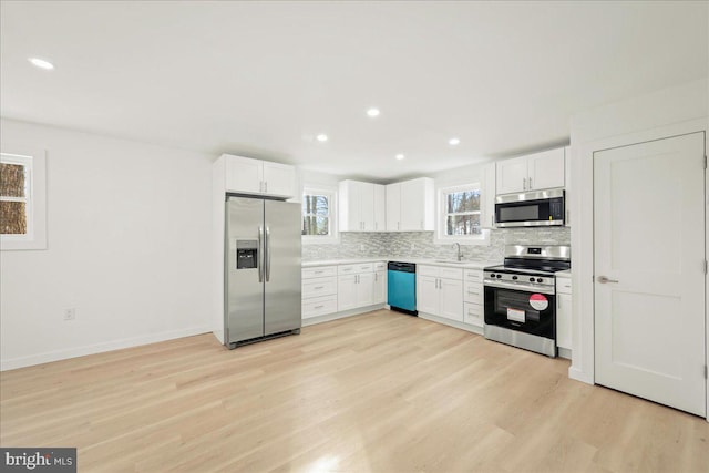 kitchen with appliances with stainless steel finishes, a sink, light countertops, white cabinetry, and backsplash