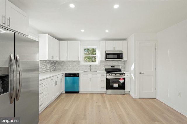 kitchen with stainless steel appliances, a sink, white cabinetry, light countertops, and backsplash