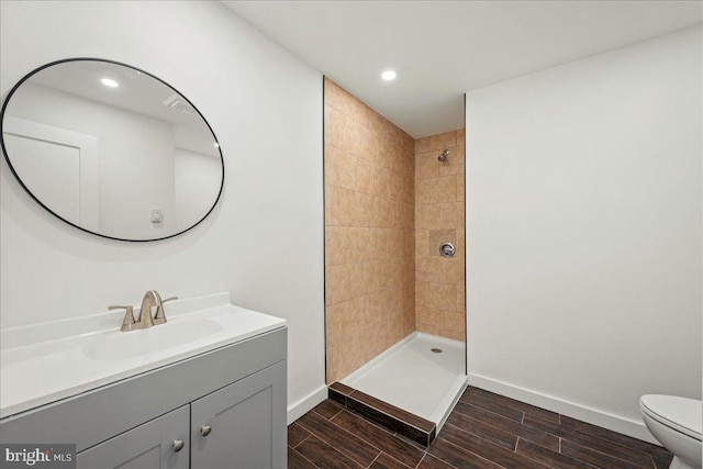 full bath featuring baseboards, tiled shower, toilet, wood tiled floor, and vanity