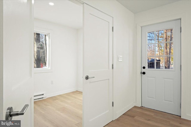 doorway featuring light wood finished floors, baseboard heating, and baseboards