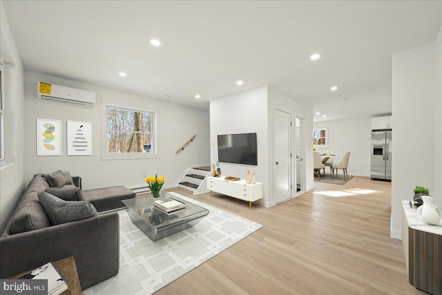 living room featuring a wall unit AC, recessed lighting, baseboards, stairs, and light wood-style floors