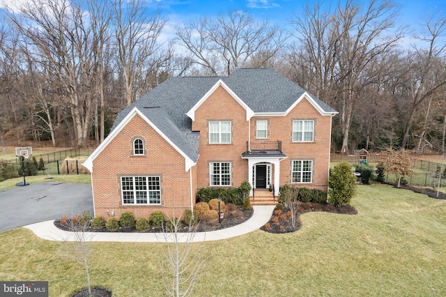 view of front facade featuring brick siding, roof with shingles, a front yard, and fence