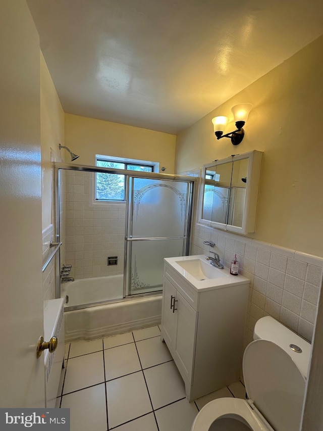 bathroom with shower / bath combination with glass door, tile walls, toilet, vanity, and tile patterned flooring