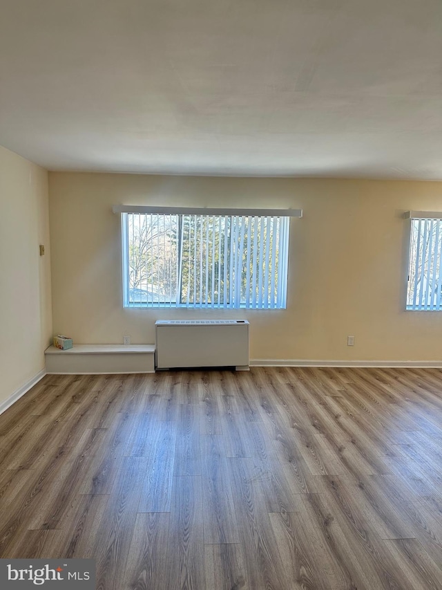 spare room with radiator heating unit, wood finished floors, and baseboards