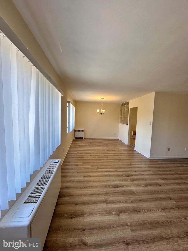 unfurnished living room featuring radiator, baseboards, a chandelier, and wood finished floors