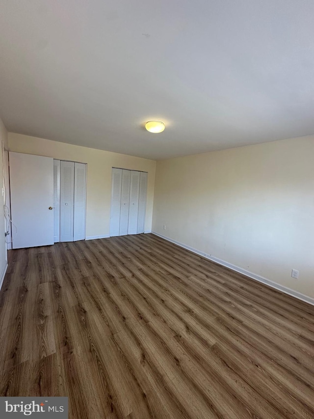 unfurnished bedroom with dark wood-type flooring, two closets, and baseboards