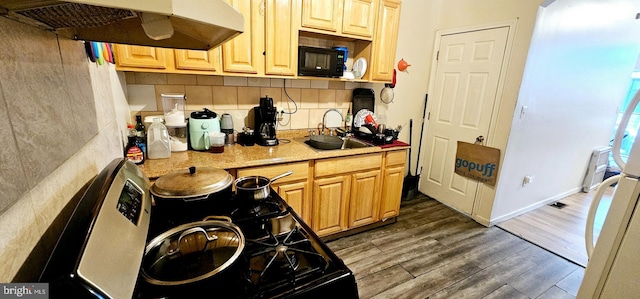 kitchen with tasteful backsplash, wood finished floors, light countertops, under cabinet range hood, and a sink