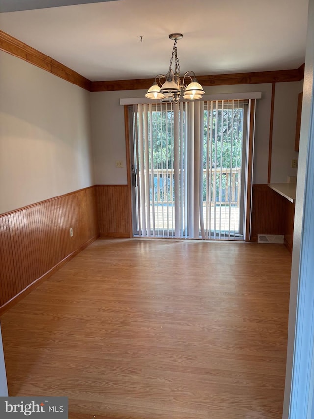 unfurnished dining area featuring wood finished floors, wainscoting, visible vents, and an inviting chandelier