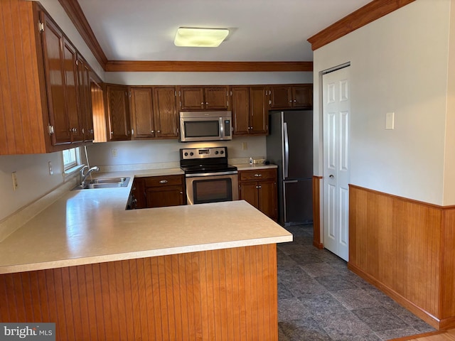 kitchen with wainscoting, stainless steel appliances, crown molding, light countertops, and a sink