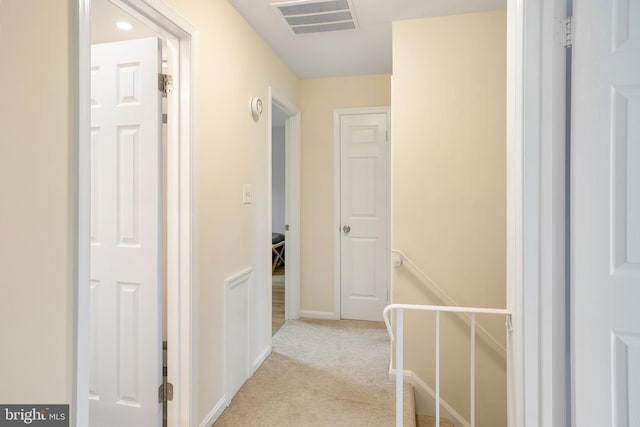 hallway featuring light carpet, visible vents, an upstairs landing, and baseboards