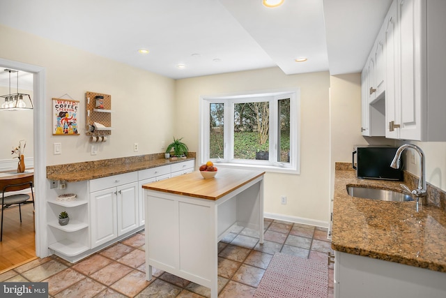 kitchen with wooden counters, open shelves, stone tile floors, white cabinetry, and a sink