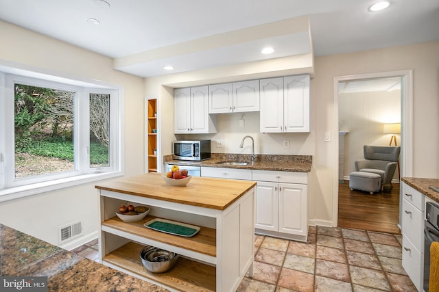 kitchen featuring stone tile floors, wooden counters, open shelves, a sink, and stainless steel microwave