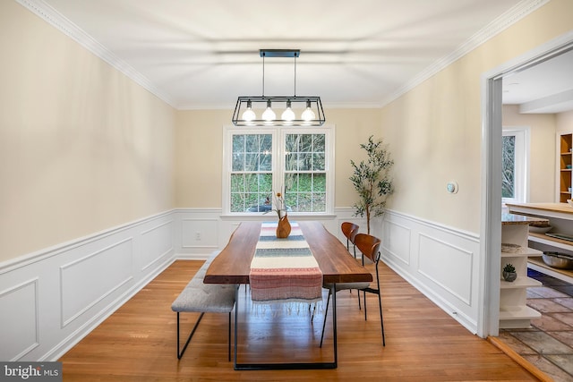 dining space featuring a wainscoted wall, ornamental molding, and light wood finished floors