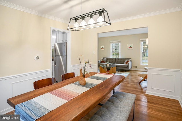 dining space with a wainscoted wall, ornamental molding, visible vents, and wood finished floors