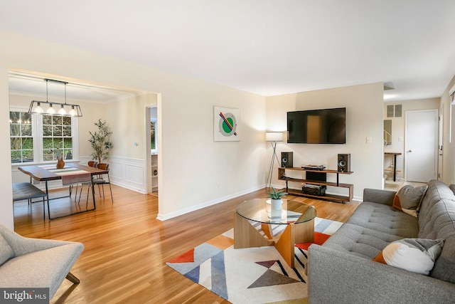 living area featuring visible vents, an inviting chandelier, wainscoting, and light wood finished floors