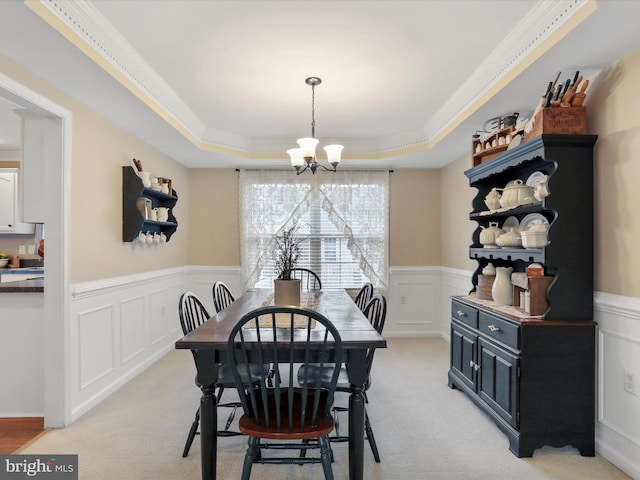 dining room with light colored carpet, a wainscoted wall, ornamental molding, a raised ceiling, and an inviting chandelier