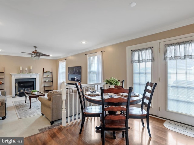 dining area with ceiling fan, light wood finished floors, a glass covered fireplace, and crown molding