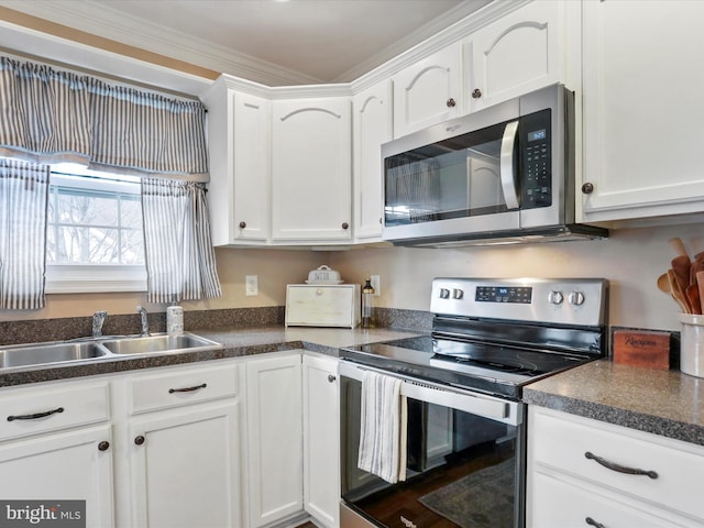 kitchen featuring dark countertops, appliances with stainless steel finishes, ornamental molding, white cabinets, and a sink