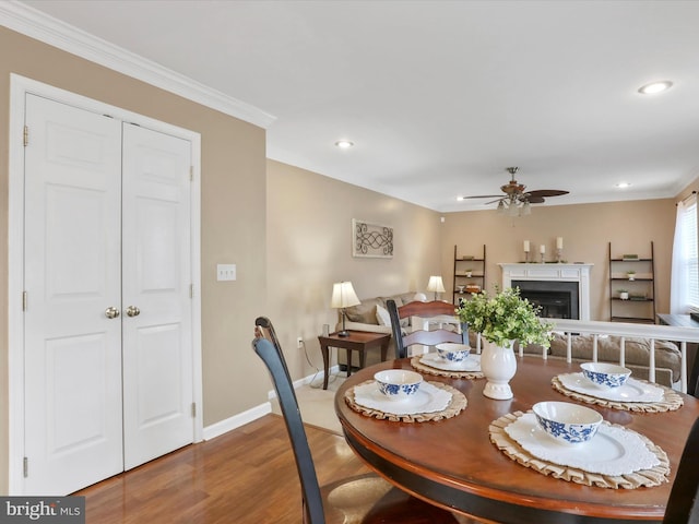 dining room with baseboards, a ceiling fan, ornamental molding, wood finished floors, and a fireplace