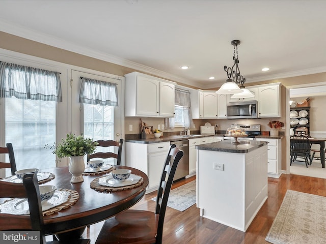 kitchen featuring decorative light fixtures, dark countertops, appliances with stainless steel finishes, white cabinetry, and a kitchen island