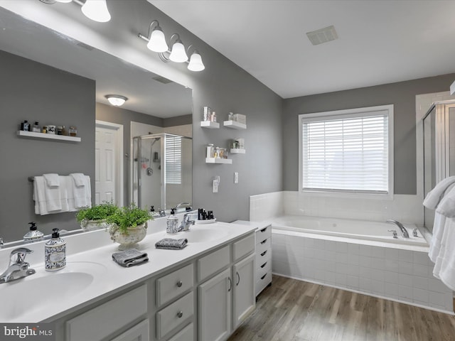 bathroom featuring a stall shower, a garden tub, a sink, and wood finished floors