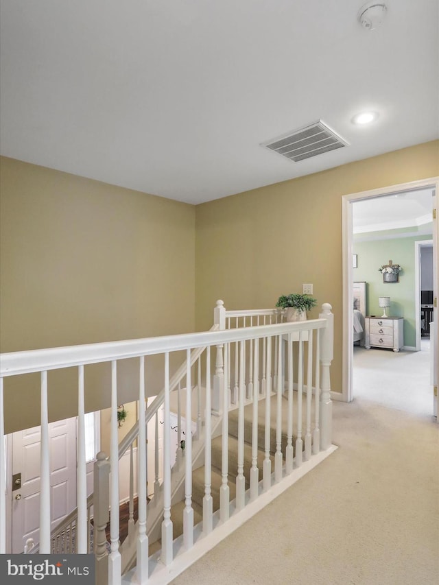 corridor featuring carpet floors, visible vents, and an upstairs landing