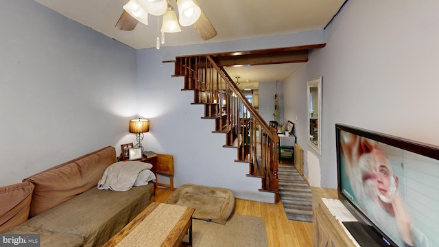 living room with light wood-style floors, ceiling fan, stairs, and beam ceiling