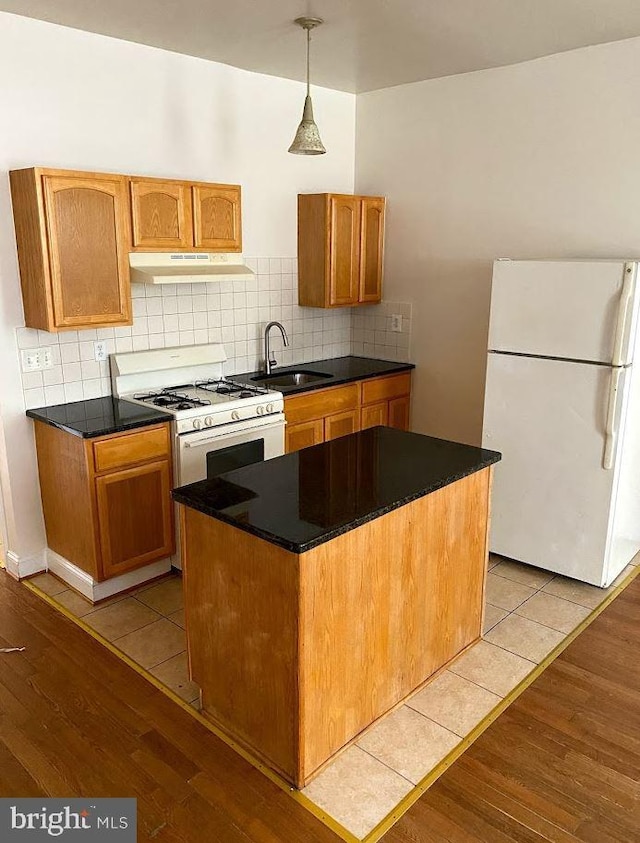 kitchen with light wood-style flooring, under cabinet range hood, white appliances, a sink, and tasteful backsplash