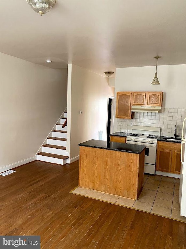 kitchen with white appliances, decorative backsplash, dark countertops, wood-type flooring, and a center island