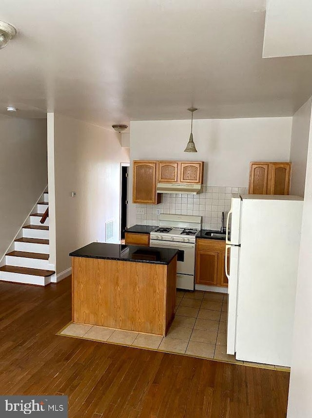 kitchen with white appliances, wood-type flooring, backsplash, and a center island