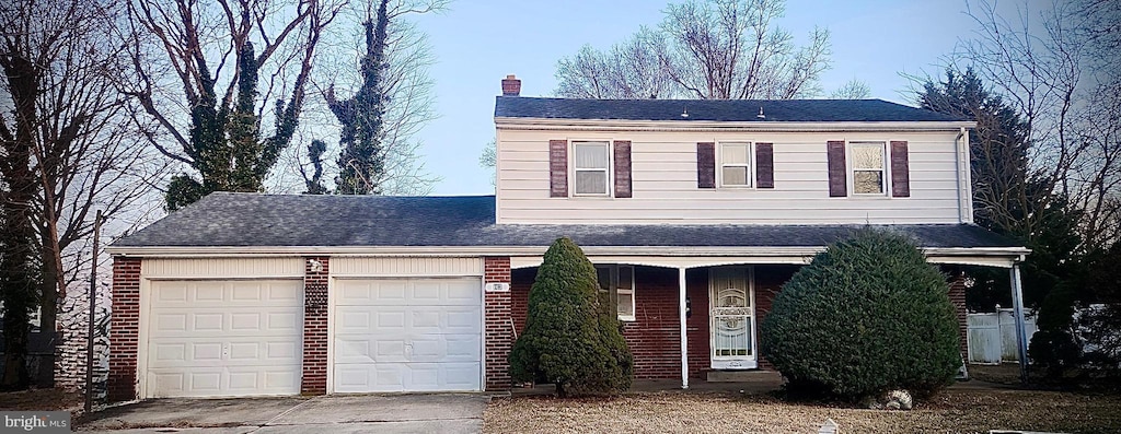 traditional-style house featuring a garage, driveway, brick siding, and a chimney