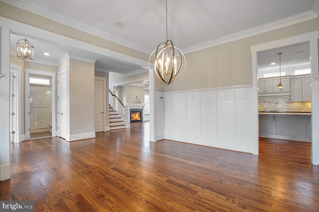 unfurnished living room with an inviting chandelier, a warm lit fireplace, crown molding, and dark wood-type flooring