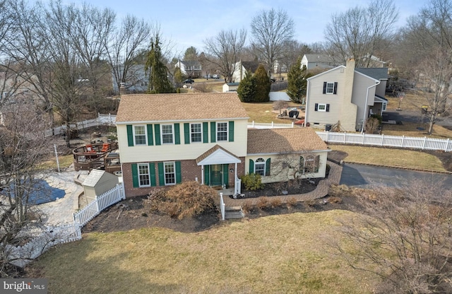 colonial-style house with aphalt driveway, fence, a front lawn, and brick siding